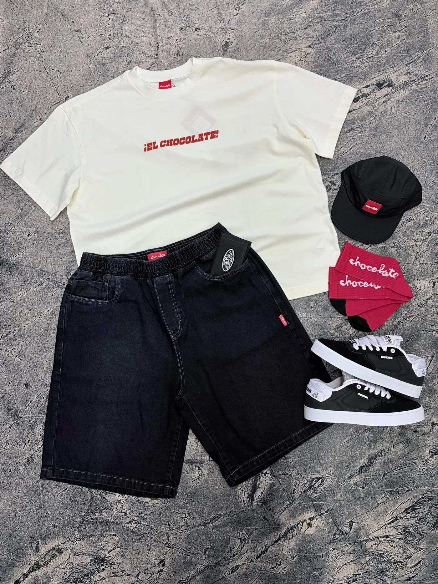 Camiseta Chocolate off-white, shorts jeans preto, boné, bandana e tênis montados no chão de concreto